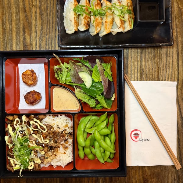A Kazoku bento box with chicken, rice, edamame, salad, fried scallops, and gyoza.