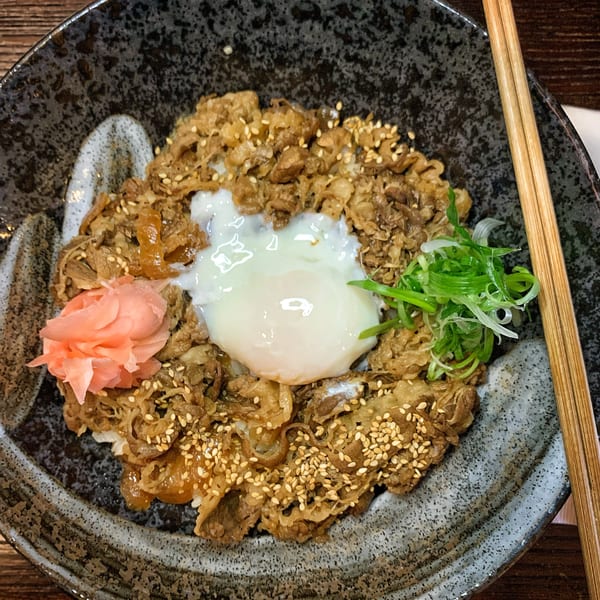 A close-up of a Gyudon bowl with beef, a poached egg, pickled ginger, and green onions.