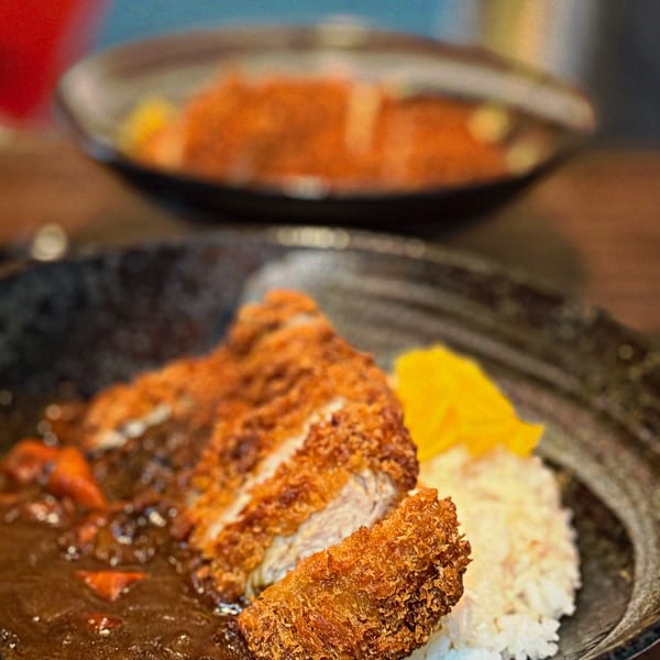 Crispy tonkatsu cutlet with rich curry sauce, white rice, and yellow pickled daikon in a black bowl.
