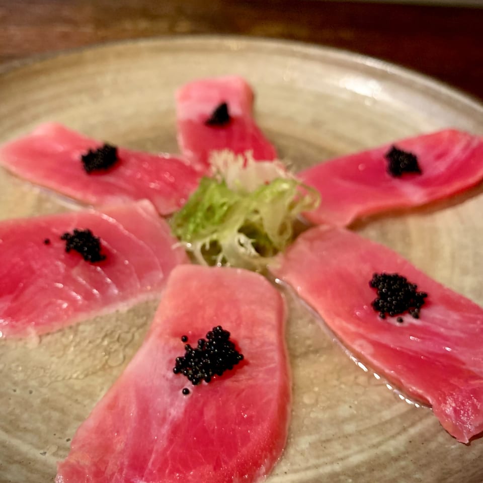 Thinly sliced tuna sashimi arranged on a plate with black caviar and shredded green garnish.