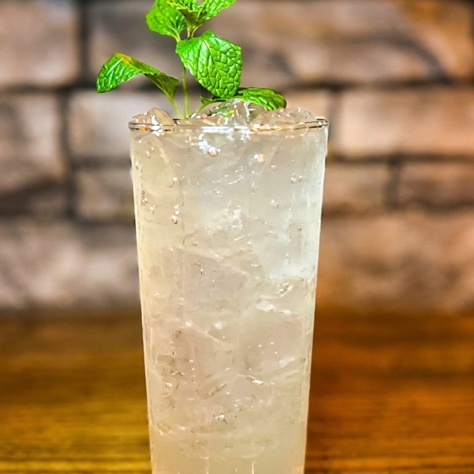 A tall glass of iced lemonade garnished with fresh mint, on a wooden table with a brick wall background.