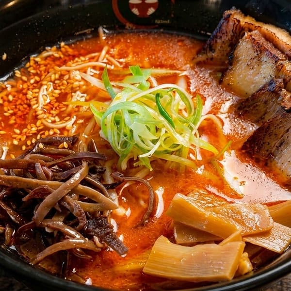 Spicy ramen in a black bowl with pork belly, bamboo shoots, wood ear mushrooms, and scallions.