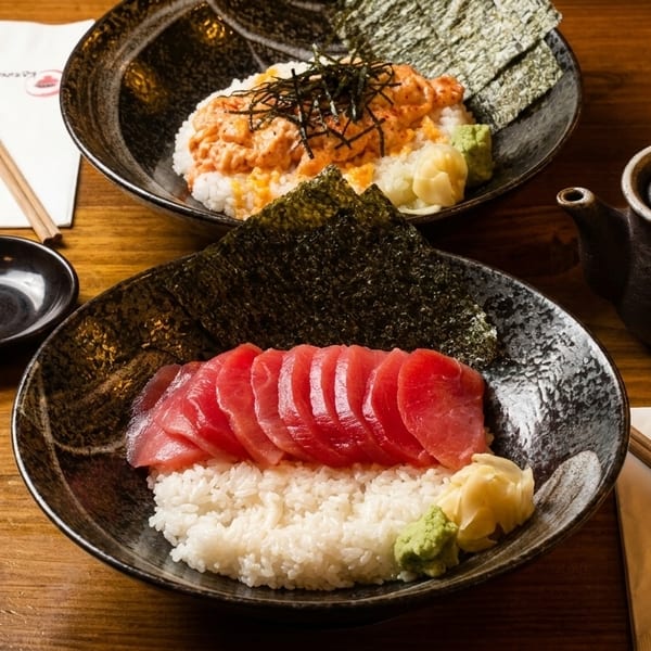 Two bowls of Japanese donburi, one with tuna sashimi and the other with spicy salmon, on a wooden table.