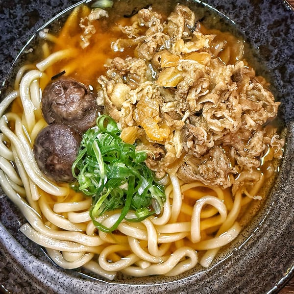 A bowl of udon noodles with beef, mushrooms, and green onions in a savory broth.